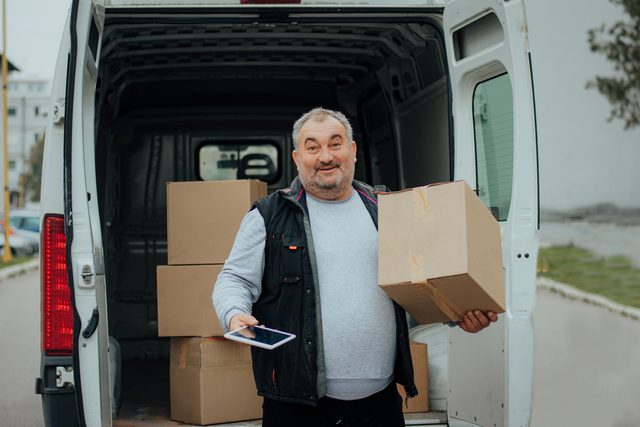 Fahrer verlädt Kartons am Heck eines Transporters